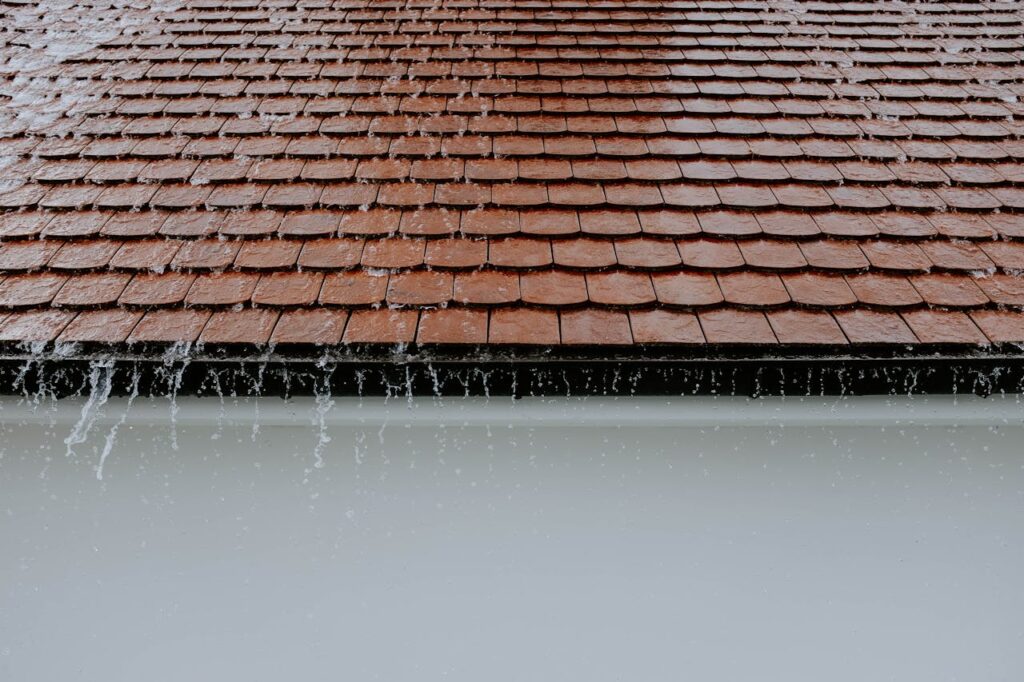 pexels-photo-2663254 Brown roof tiles with rainwater cascading down, showcasing architectural texture and detail.